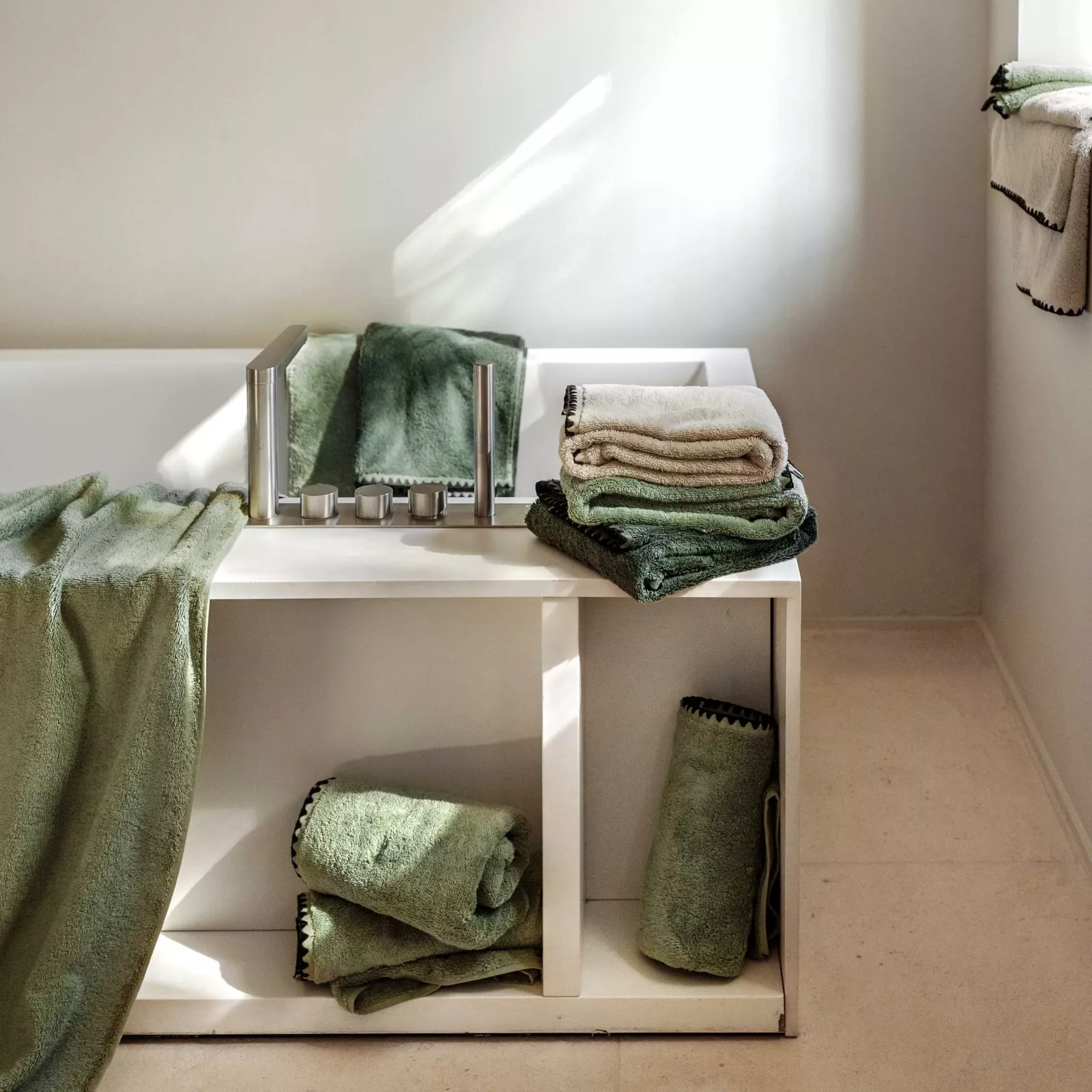 Serviettes de bain Haomy vert sauge disposées autour d’une baignoire moderne dans une lumière naturelle.